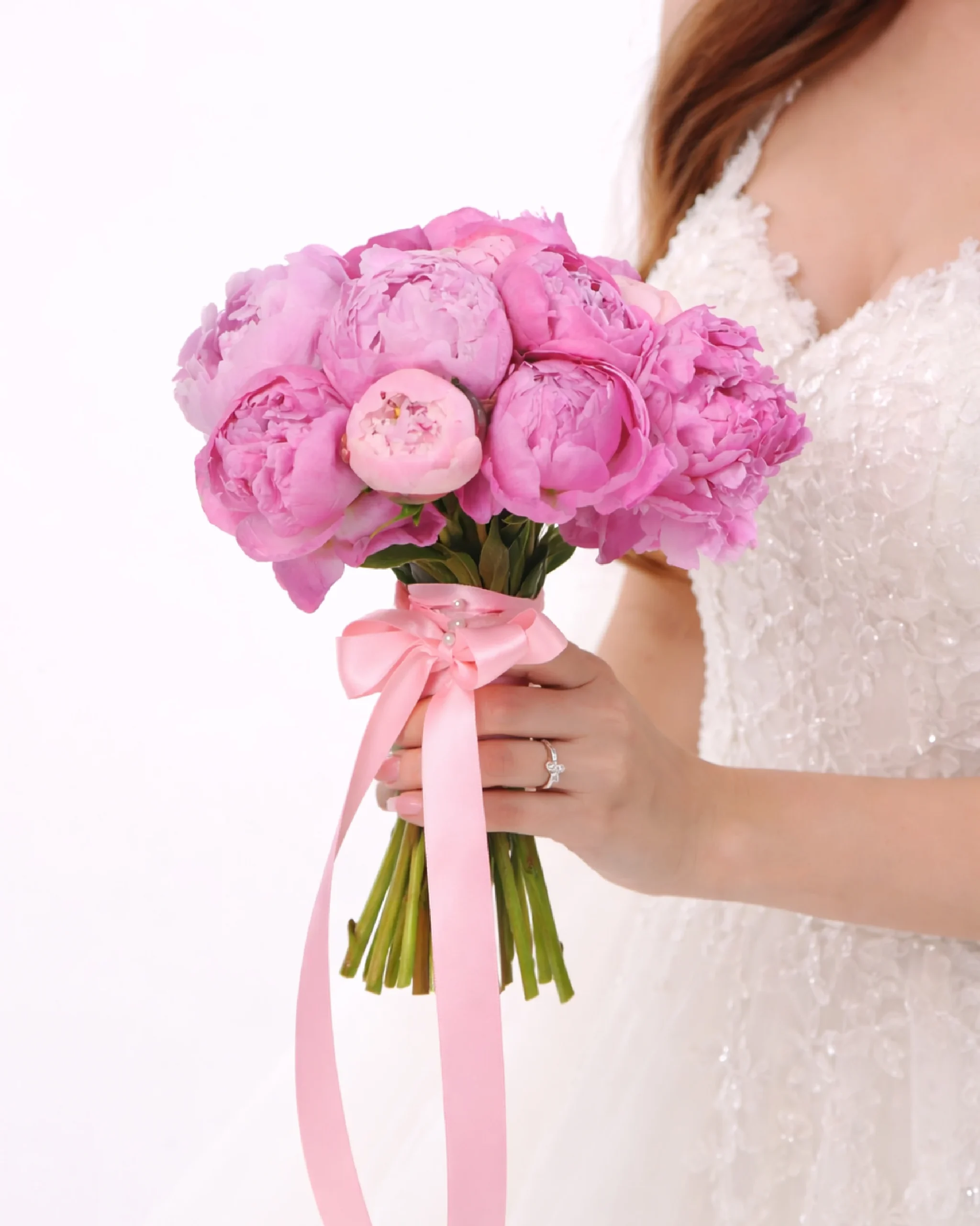 Elegant pink peony bridal bouquet with soft ribbon held by a bride in a wedding dress