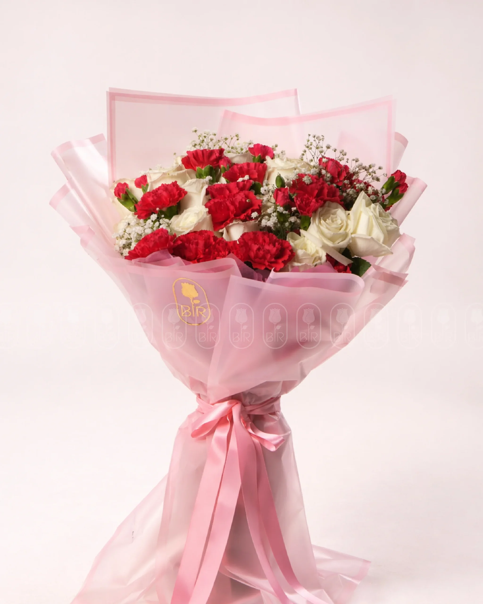 Elegant bouquet of red carnations and white roses beautifully wrapped in luxury pink floral paper