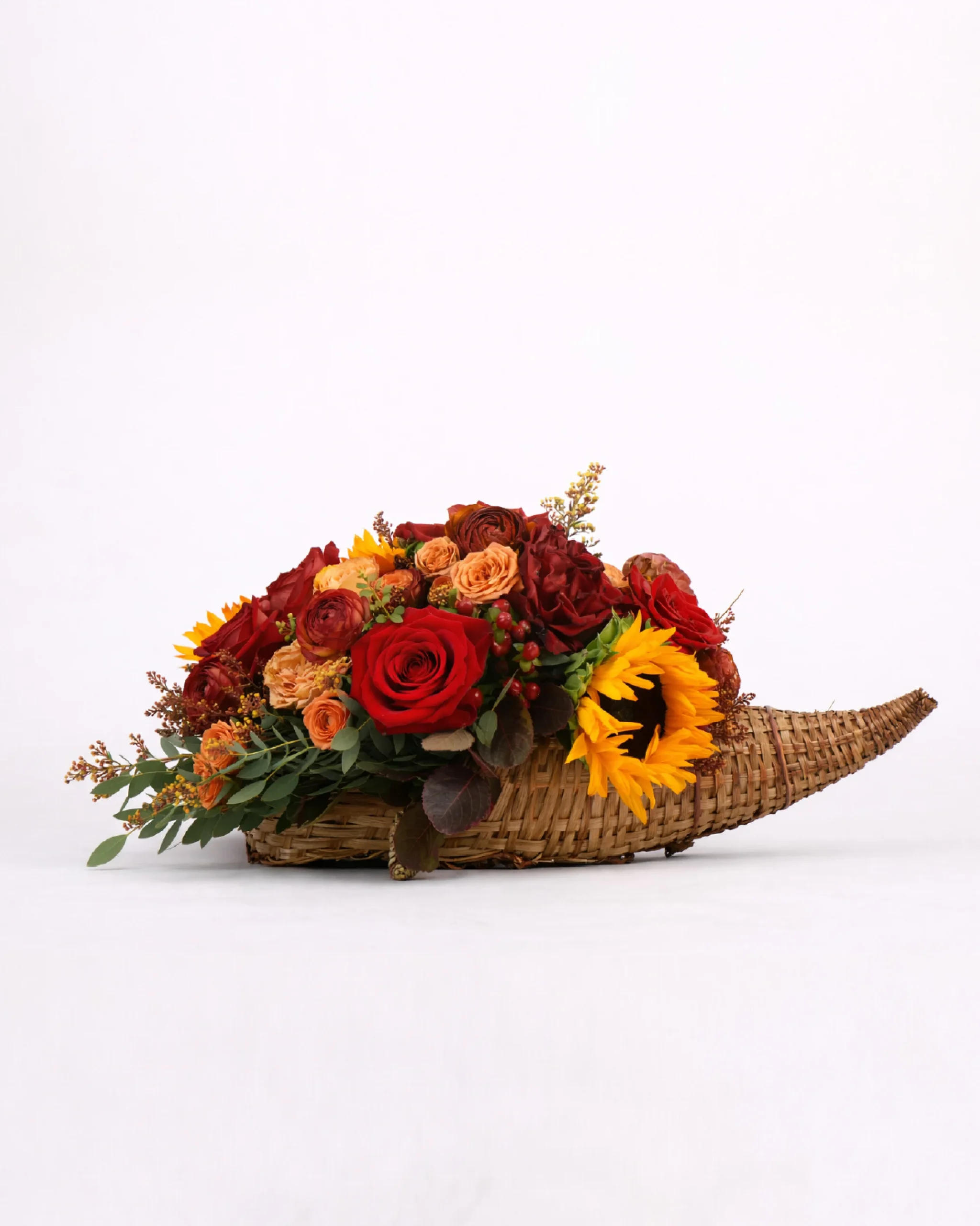 Autumn flower arrangement with red roses and sunflowers in a woven cornucopia basket