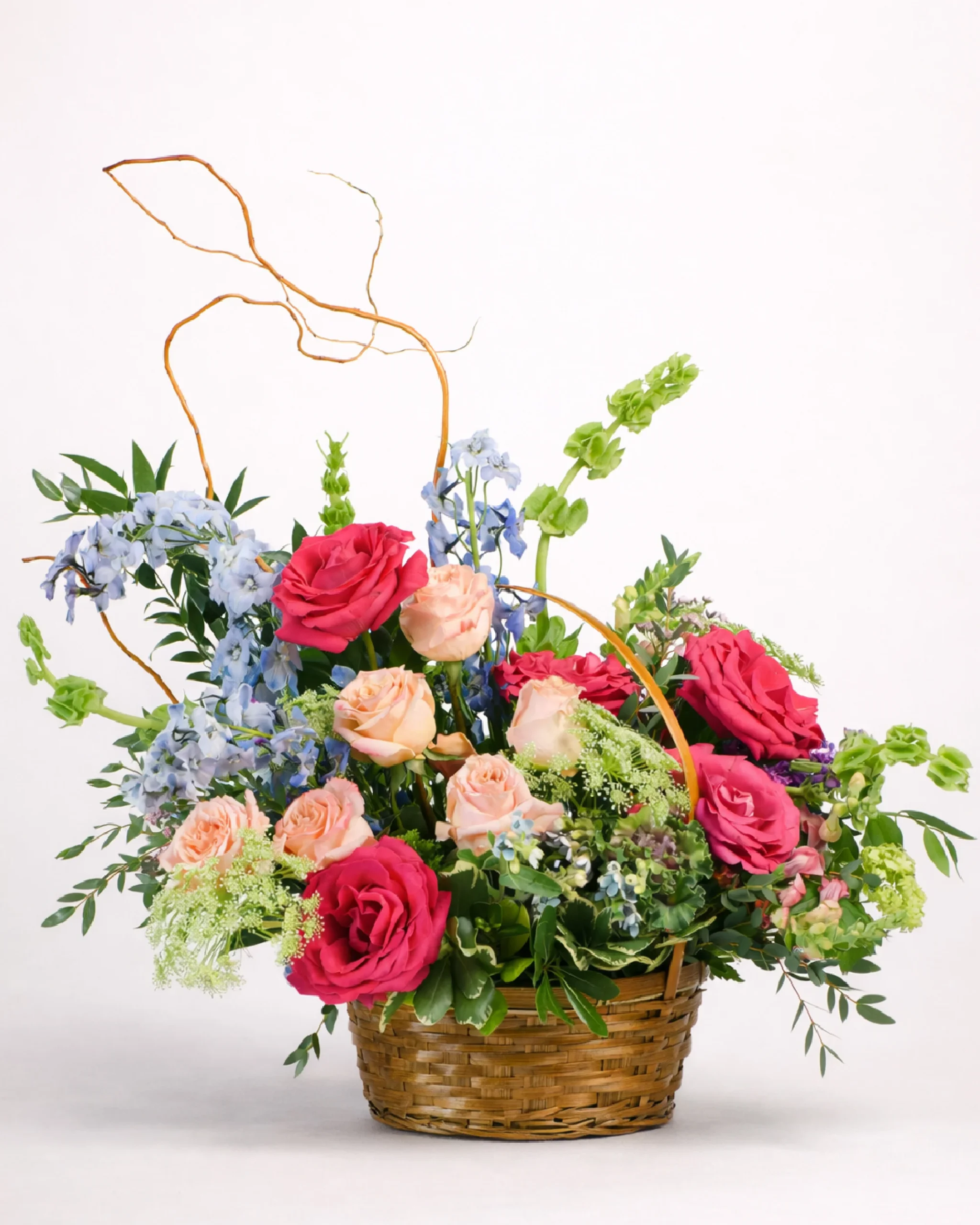 Designer flower arrangement in a basket with pink, blue, and peach blooms