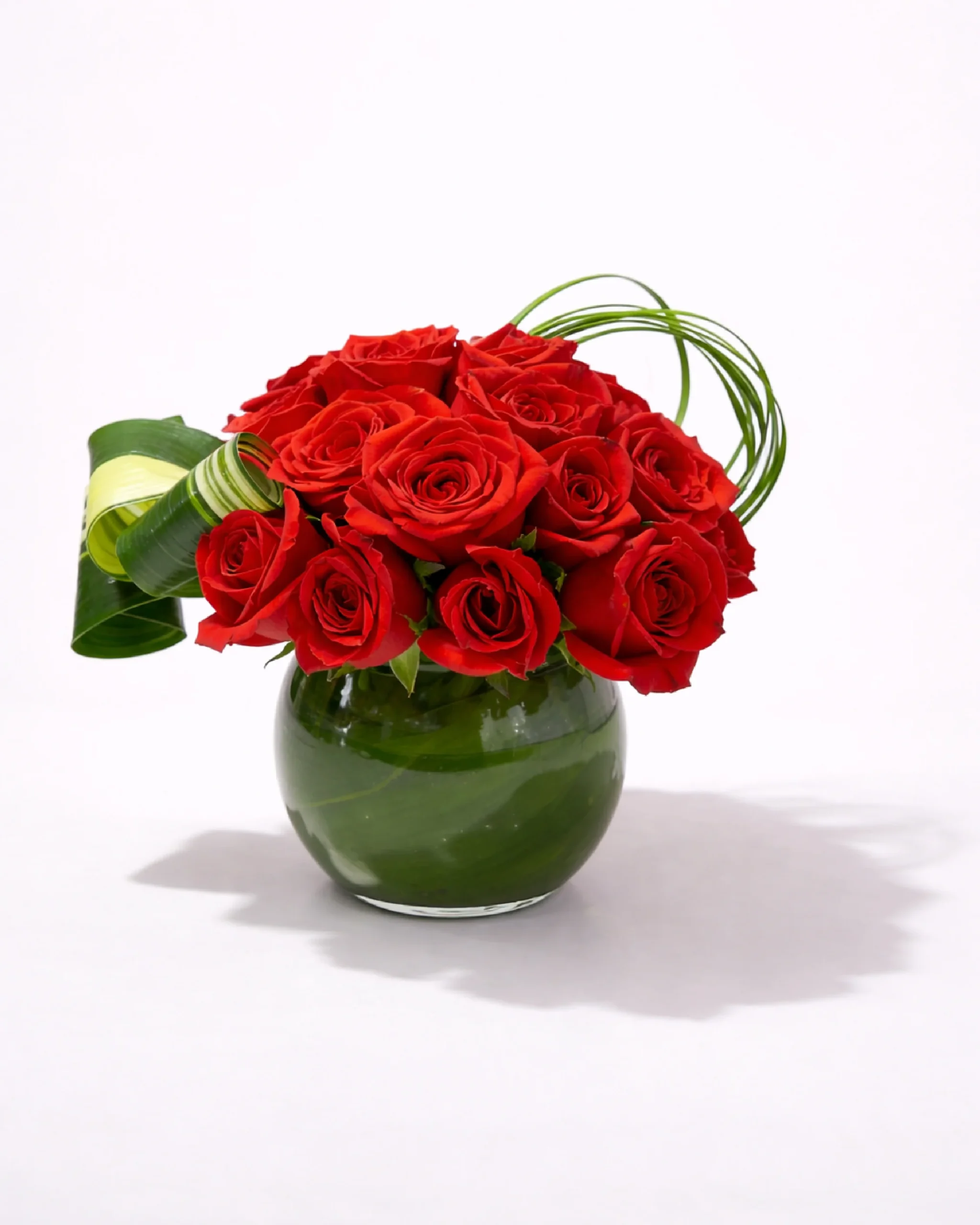 Compact arrangement of red roses in a round glass vase with green leaf accents