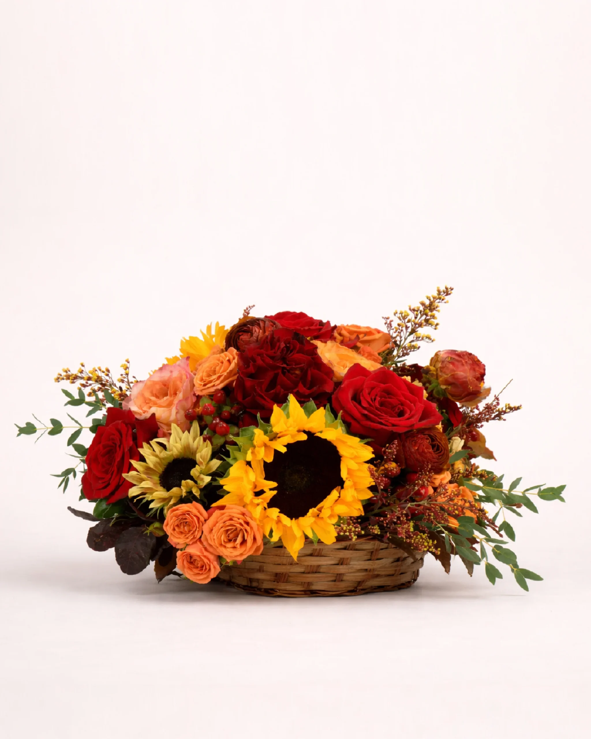 Autumn basket arrangement with sunflowers, red roses, and orange flowers
