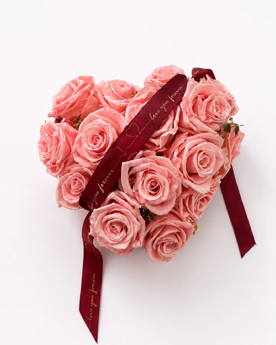 Heart-shaped arrangement of soft pink roses with burgundy ribbon