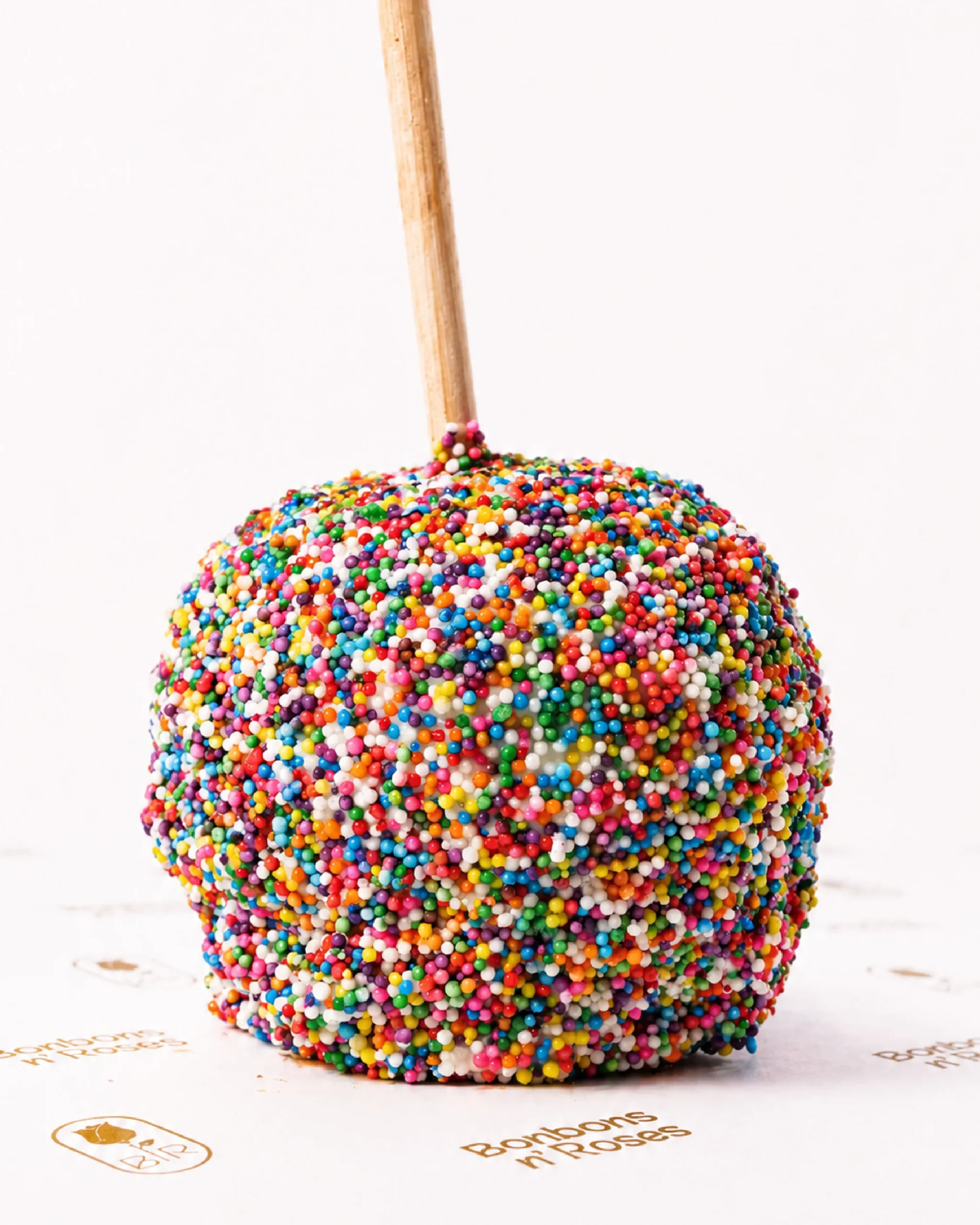 Handcrafted gourmet caramel apple coated with colorful rainbow sprinkles over premium chocolate.