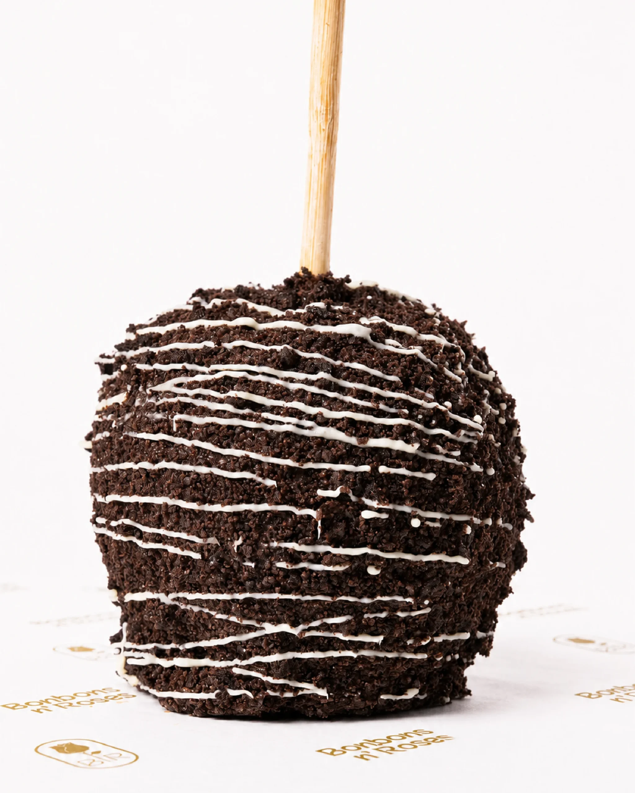 Handcrafted gourmet caramel apple coated with dark chocolate cookie crumbs and finished with a white chocolate drizzle.